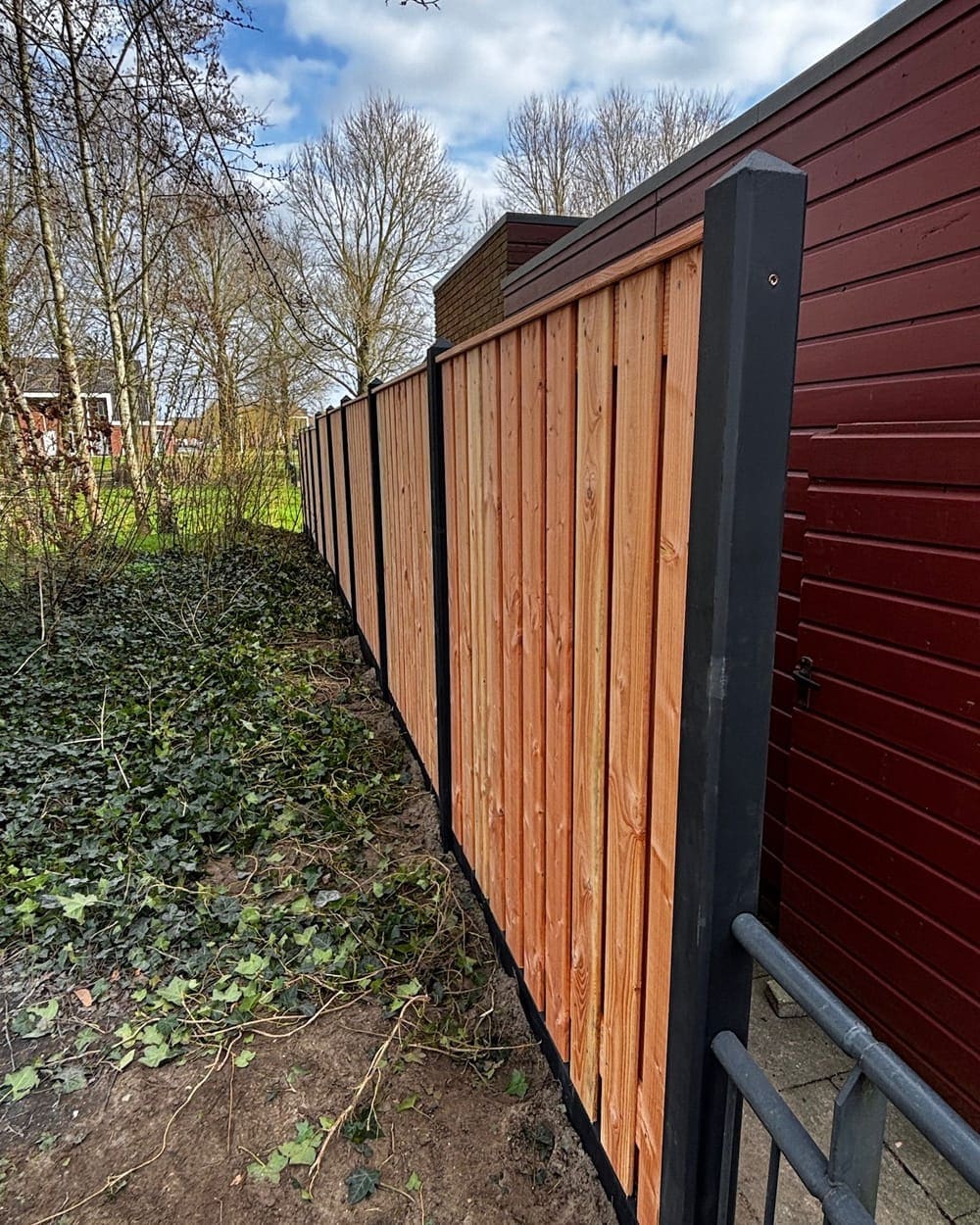 Dezelfde tuin na plaatsing, met een nieuwe houten schutting op betonpalen