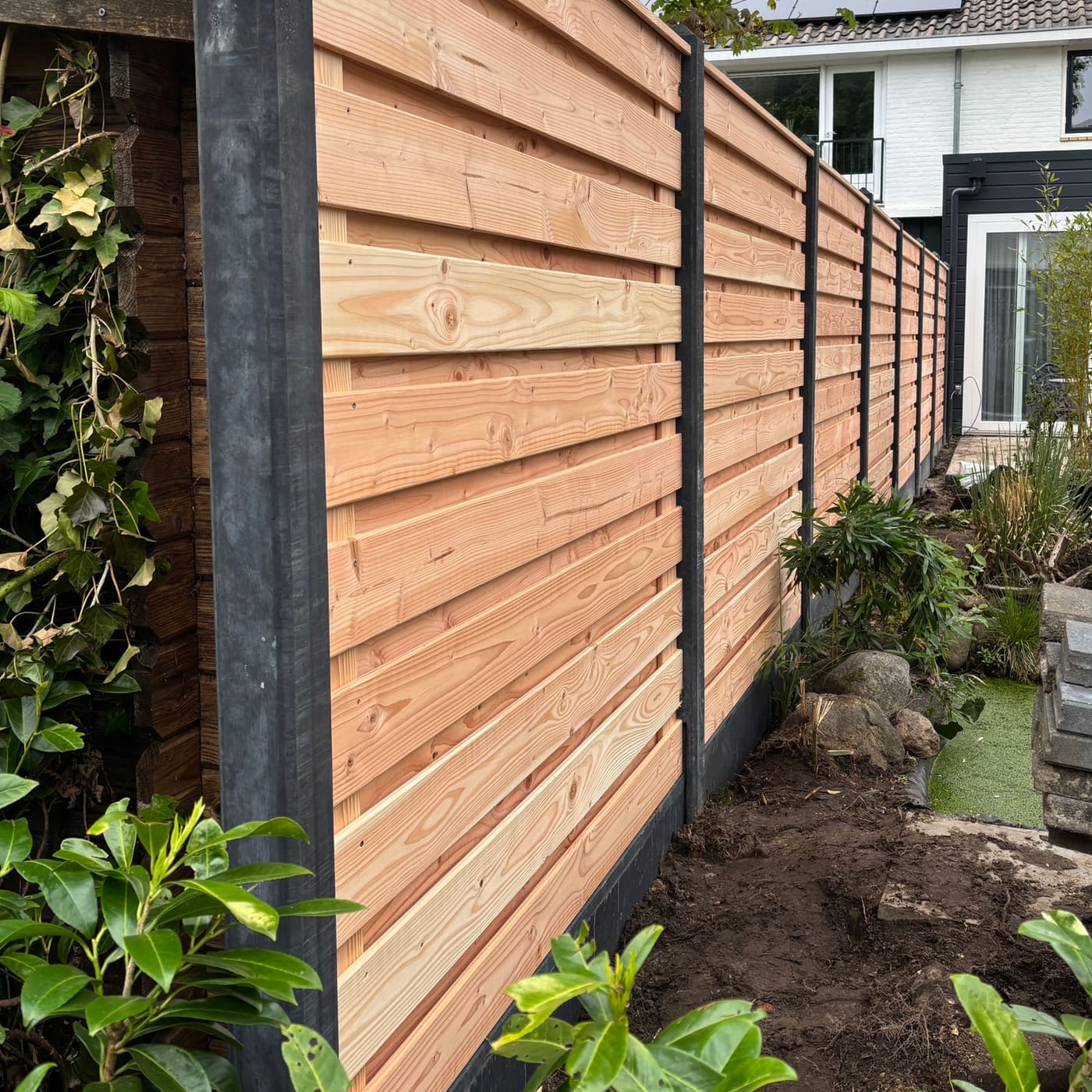 Houten schutting met betonpalen langs een tuinpad